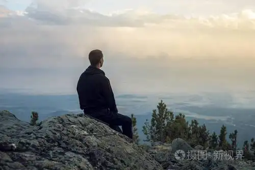 男人正坐在一个石头的山坡上,手查看该视图从高地和享有自由