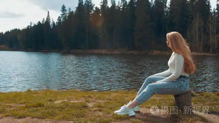 美丽的年轻金发女人坐在湖边的公园里放松侧视图