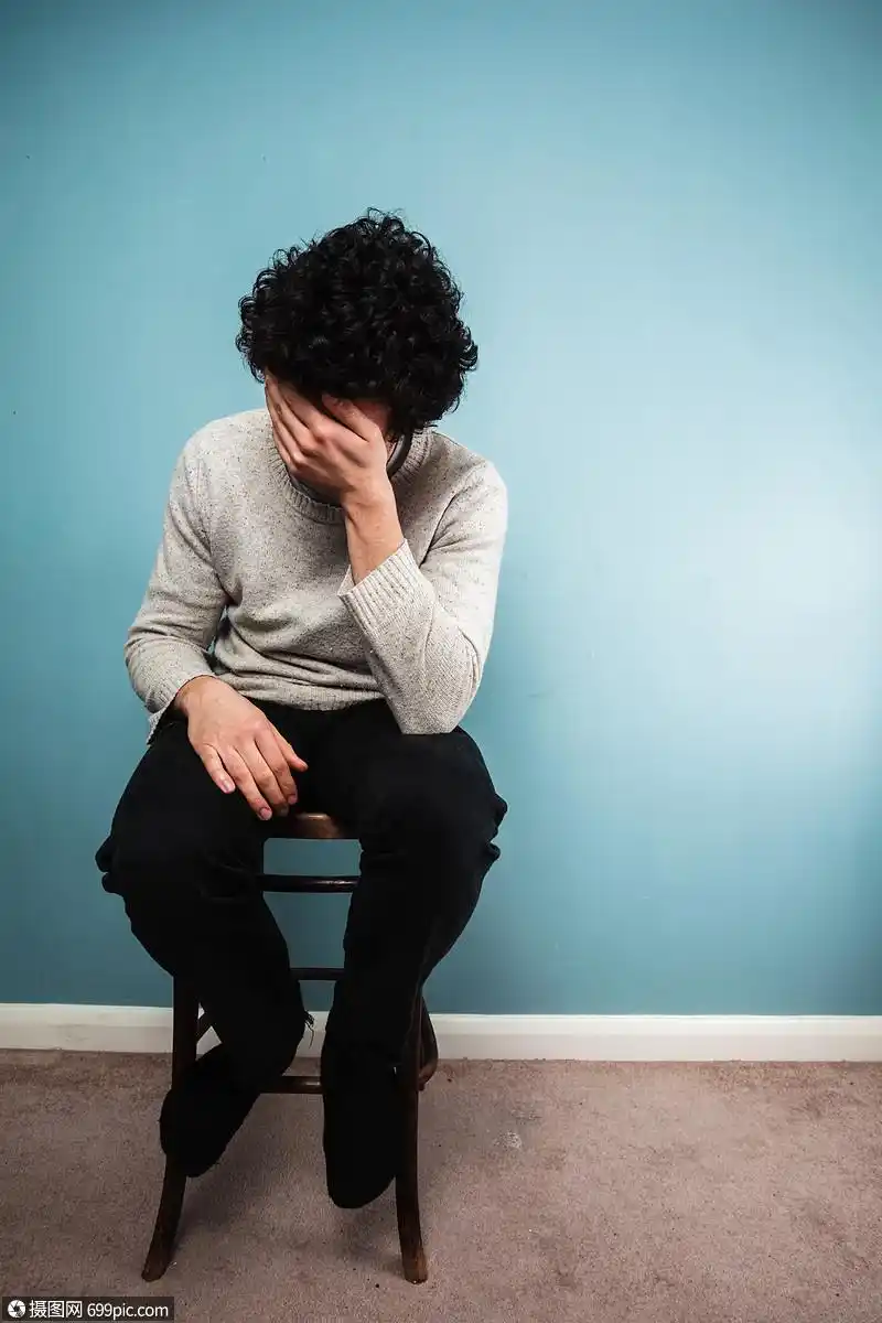 个悲伤的轻人坐蓝色墙边的高椅子上