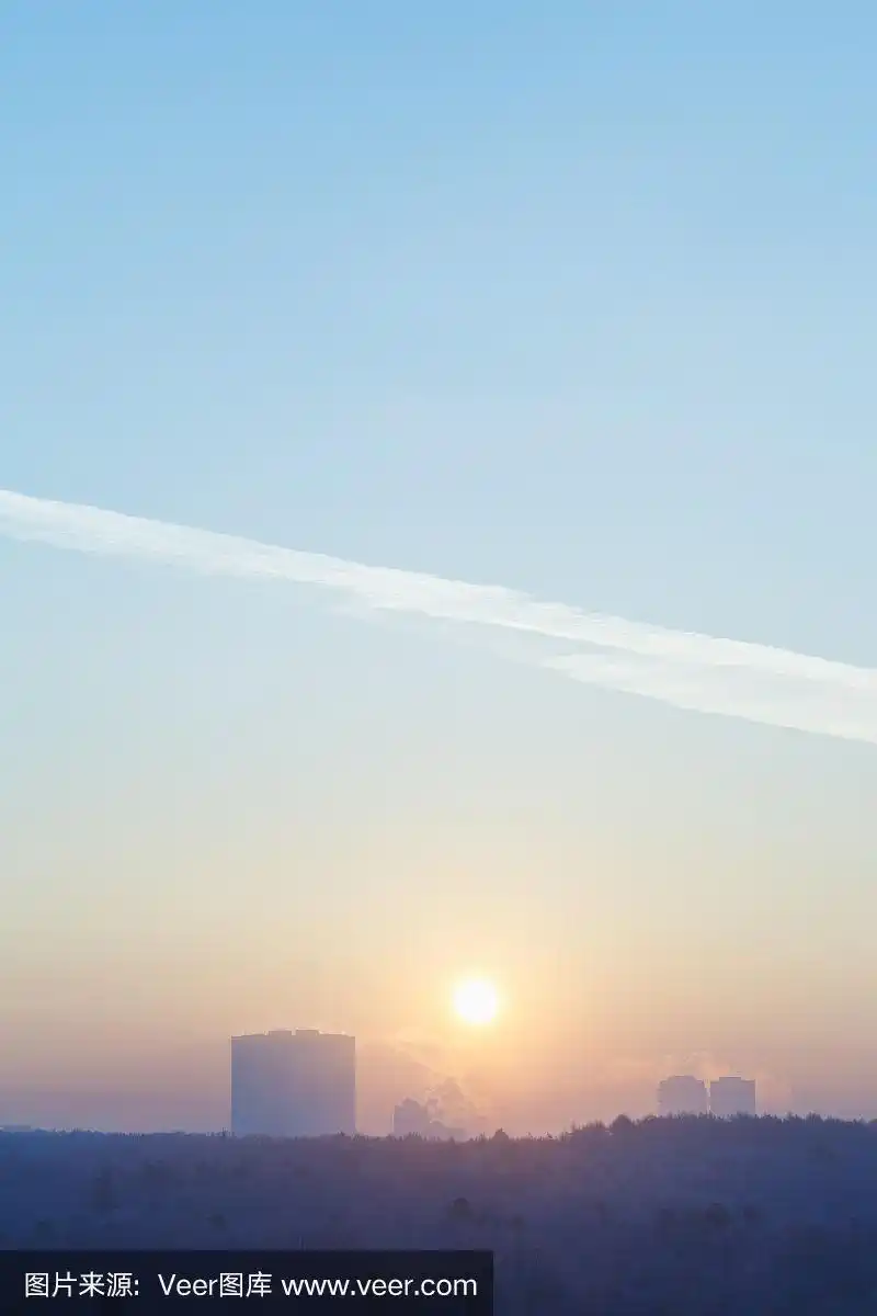 在寒冷的冬天,太阳在城市上空的蓝天中升起
