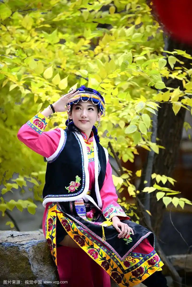 身穿少数民族服装的少女坐在树下不注视镜头