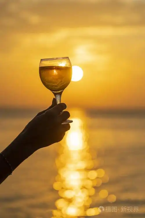 女人手拿酒杯,对着美丽的日落在热带海滩上,近距离拍摄.