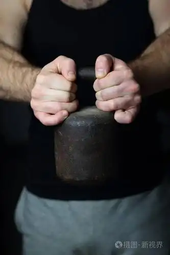 和运动裤的男人粗暴地用强壮的双手握着一个老式的重量,作为运动力量