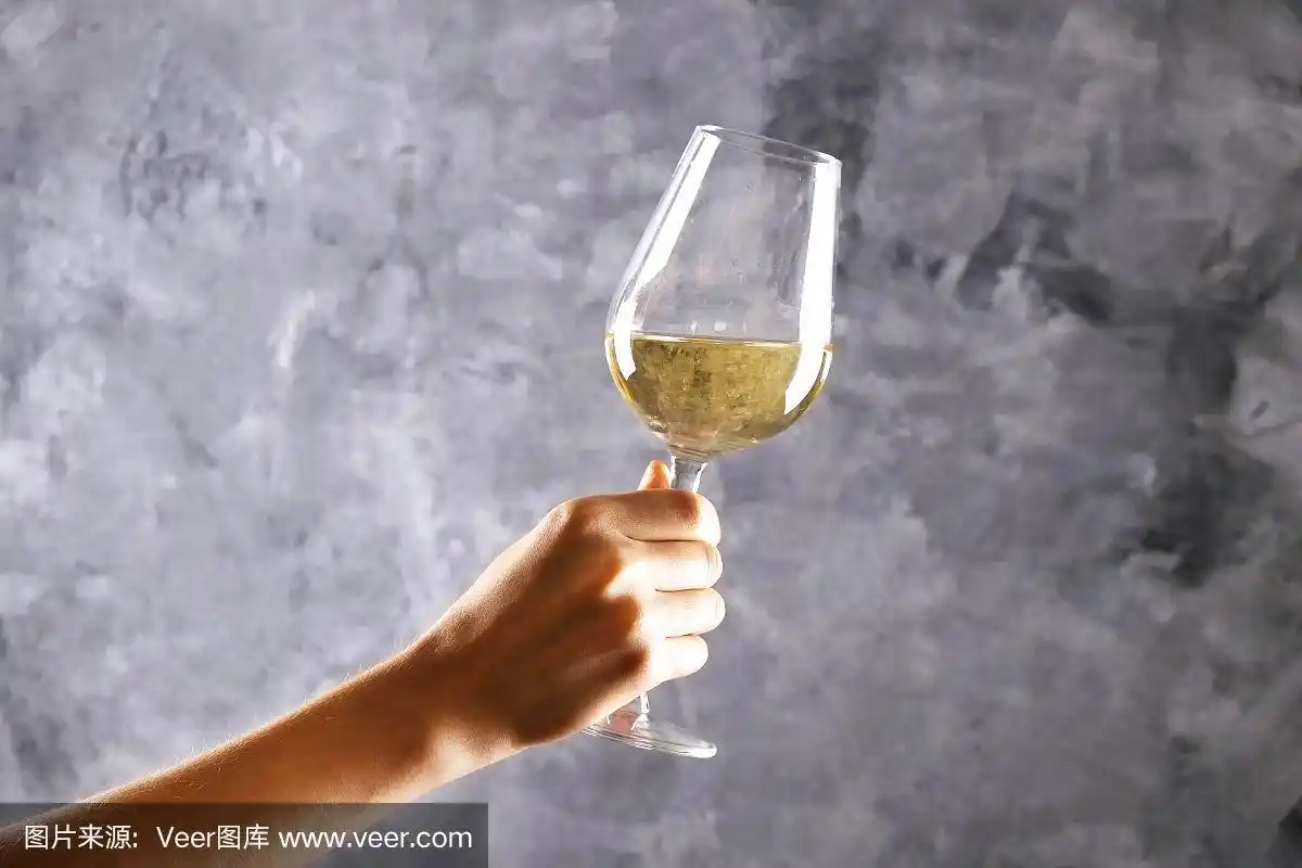 剪短的镜头年轻女子的手拿着一杯白葡萄酒在灰色的背景.