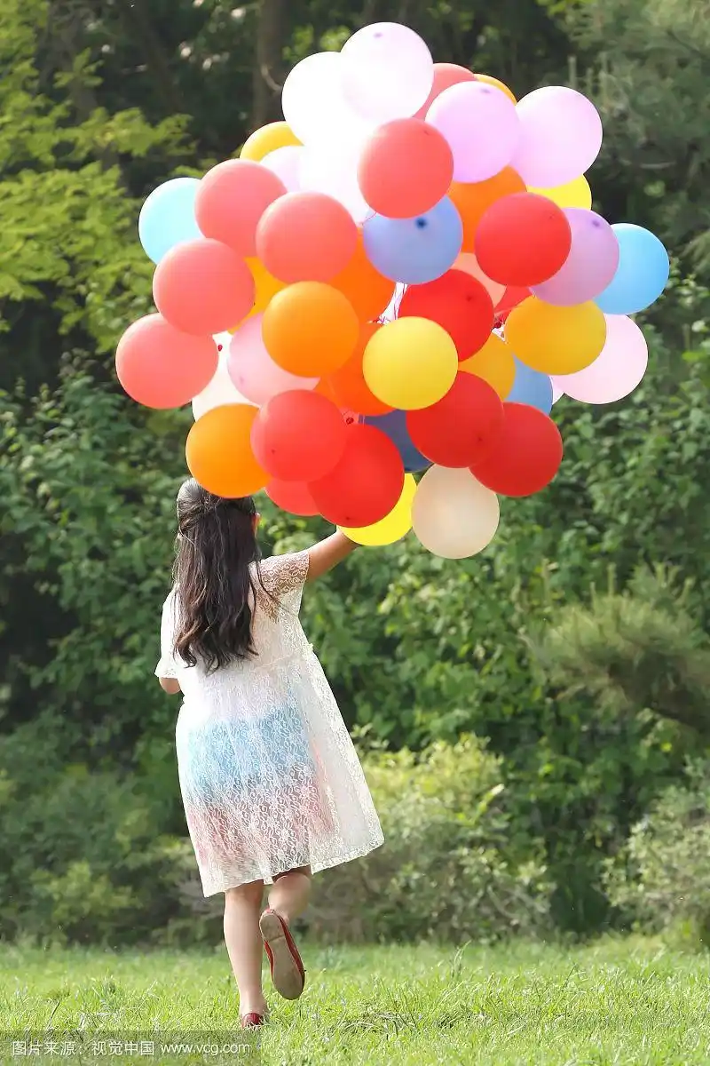 小女孩拿着气球在草地上奔跑