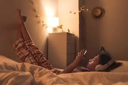 晚上躺在床上用手机听音乐的少女照片