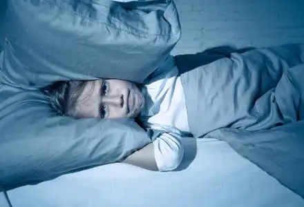 不快乐的女孩覆盖她的耳朵与枕头试图睡在晚上感到不眠之夜悲伤和疲惫