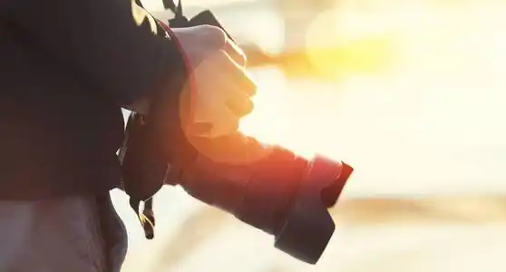 在阳光下,男人用手拿着相机.概念专业旅行生活摄影师照片