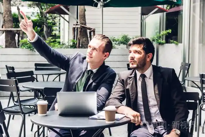 两个穿黑色西装的商人同事在咖啡馆里交谈和工作,一起讨论一些事情.