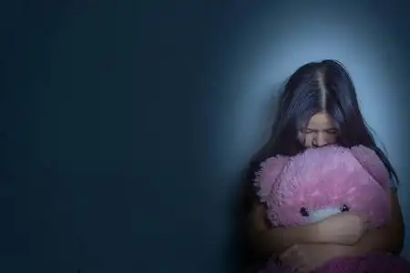 膝盖黑一个悲伤的女人抱着她的膝盖哭着坐在黑暗中的泰迪熊照片