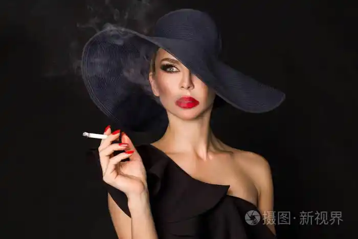 优雅的女人,黑党徽与香烟在手拿着帽子.在黑色背景上