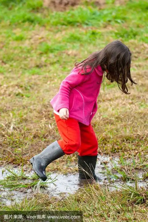 小女孩穿着雨靴在泥地里玩耍